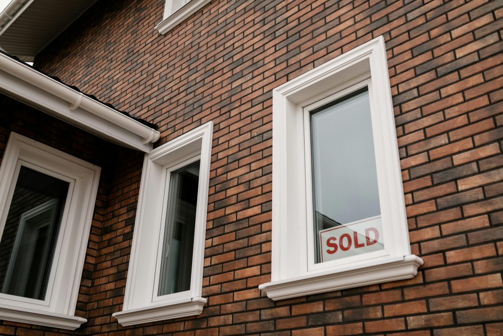 pexels photo 7641828 7641828 Close-up of a brick house with a 'Sold' sign in the window, showcasing real estate sales.